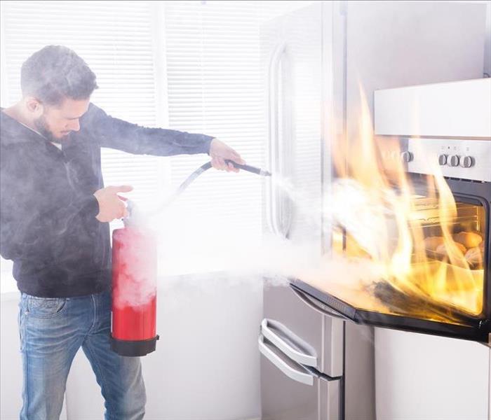 Image of a person using a fire extinguisher in a oven fire. 