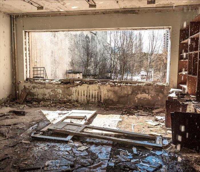 Image of a room damaged with contaminated water after a severe storm. The floor, walls and window have mud and debris. 